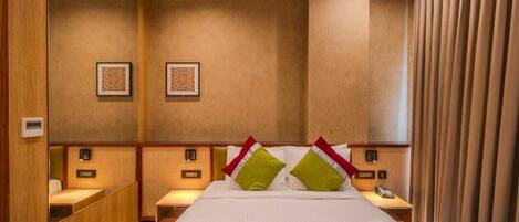 A hotel room with a large bed, two bedside tables, a mirror, and a wall-mounted telephone.
