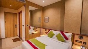 Une chambre d’hôtel avec un grand lit, une armoire en bois, un miroir et une table de chevet avec une lampe.