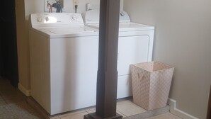 A laundry area with a washing machine, a drying rack, and a brick pillar.