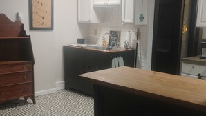 A compact kitchen with white cabinets, a wooden dining table, and a patterned rug.