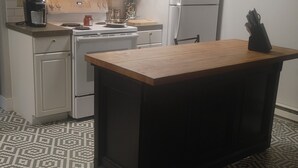 A kitchen with white cabinets, a microwave, a stove, a refrigerator, and a wooden island.