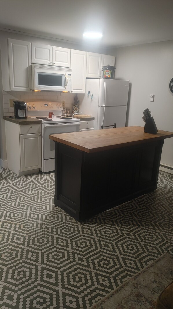 A kitchen with white cabinets, a microwave, a stove, a refrigerator, and a wooden island.