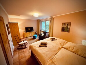 Een slaapkamer met een bed, een bureau met een televisie, een stoel en een raam met gordijnen.
