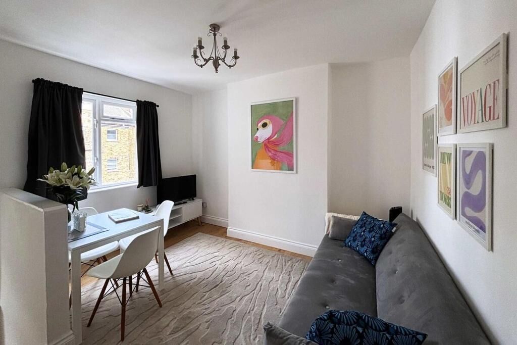 A living room with a grey sofa, a dining table with chairs, a TV, and artwork on the walls.