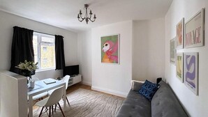 Una sala de estar con un sofá gris, una mesa de comedor con sillas, un televisor y obras de arte en las paredes.