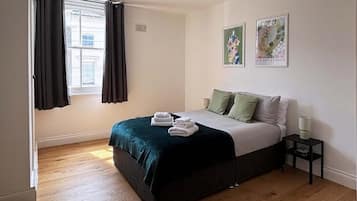 A bedroom with a bed, a nightstand, a window with curtains, and two wall art pieces.