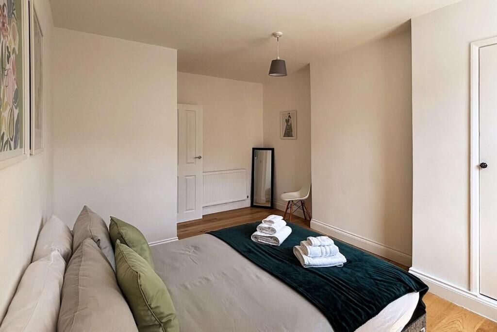 A bedroom with a bed, pillows, a bedside table with towels, a chair, and a door.