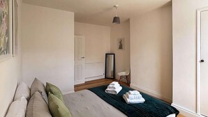 Un dormitorio con cama, almohadas, una mesita de noche con toallas, una silla y una puerta.