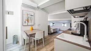 Cozinha compacta com área de refeições, uma cama ao fundo e unidade de ar condicionado visível.
