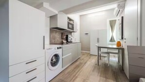Uma cozinha compacta com máquina de lavar, área de refeições e uma mesa pequena.