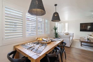 Een eethoek met een houten tafel, zwarte stoelen en een geweven hanglamp.
