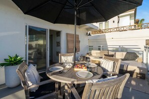 An outdoor patio with a round wooden table set for dining, surrounded by wooden chairs. - Oceanview Luxe Home | Steps to the Strand | Bikes (Manhattan Beach)