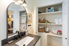 A bathroom with a large mirror, a sink, and shelves with towels and toiletries. - Oceanview Luxe Home | Steps to the Strand | Bikes (Manhattan Beach)