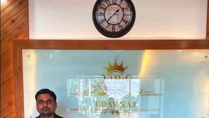 A reception desk with a clock above it, a glass partition with a logo, and a wooden wall. - Hotel Uday Raj (Agra)