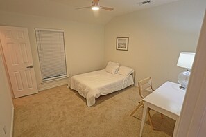 A bedroom with a single bed, a chair, a desk, a window with blinds, and a ceiling fan.