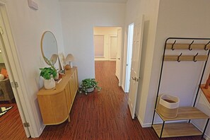 A hallway with a wooden dresser, a mirror, a lamp, a plant, and a coat rack.