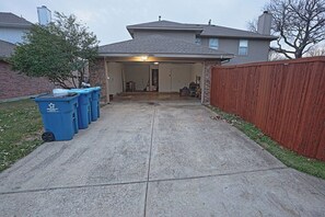A garage with a concrete driveway leading to a house. There are blue recycling bins lined up against the garage wall.