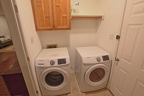 A laundry room with two front-loading washing machines, wooden cabinets above, and a door to the right.