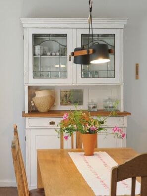 Een keuken met witte kastjes, een houten aanrecht, een hangende lamp en een tafel met een bloemenarrangement.