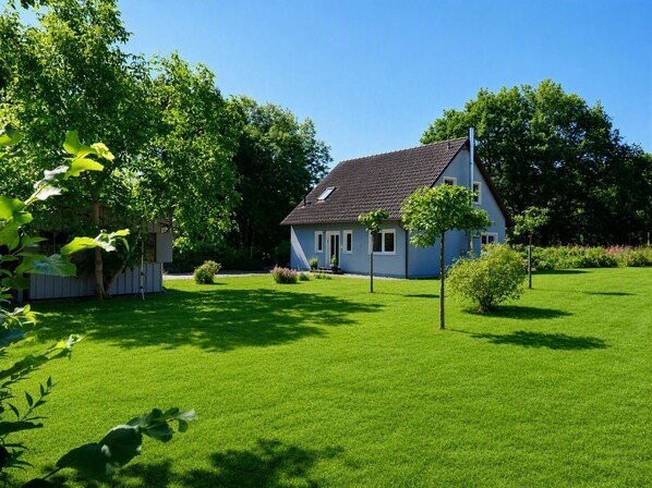 Een huis met een schuin dak, omgeven door een verzorgd gazon en bomen.