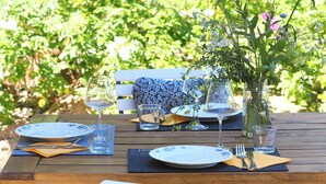 Ein Holztisch ist gedeckt mit blauen und weißen Tellern, klaren Gläsern und einer Vase mit Blumen.