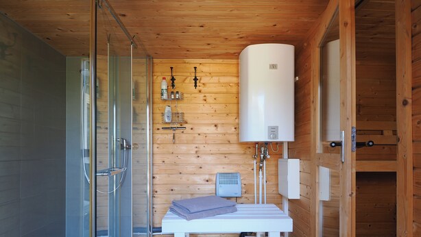 Ein Badezimmer einer Holzhütte mit einer Duschkabine aus Glas, einer weißen Sitzbank und einem großen, weißen Boiler.