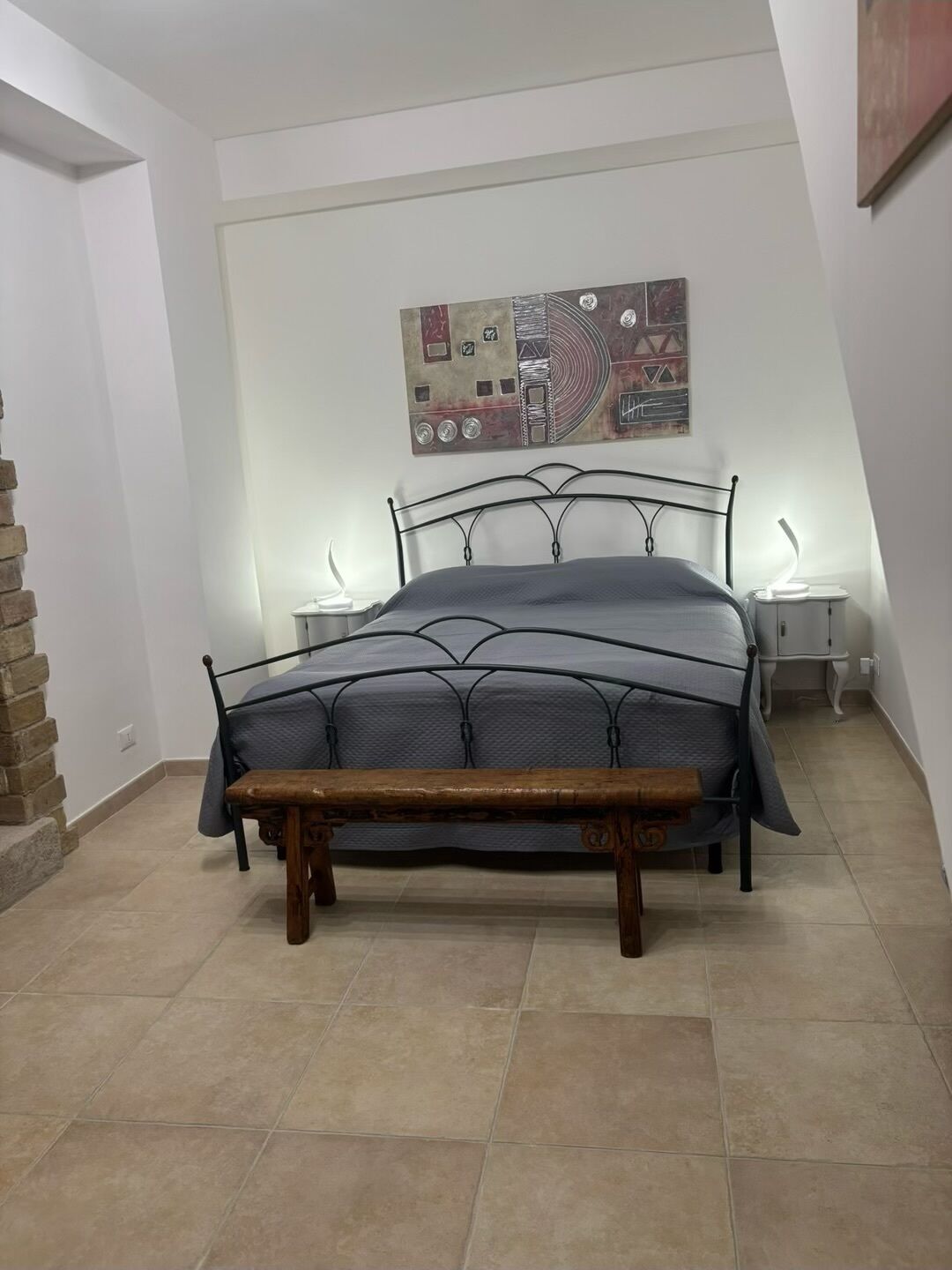 Ein Schlafzimmer mit Bett, einer Bank, einem Wandbild und einer Ziegelwand.