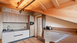 A modern kitchen with wooden cabinets, a microwave, and a dining table with chairs. - Chalet 'Malva' with Mountain View, Balcony and Wi-Fi (Livigno)