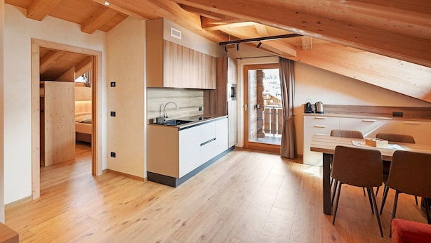 A modern kitchen with wooden beams, a dining area with chairs, and a view through a glass door. - Chalet 'Malva' with Mountain View, Balcony and Wi-Fi (Livigno)