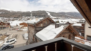 A wooden cabin with a snow-covered roof, a view of a ski slope, and a town in the background. - Chalet 'Malva' with Mountain View, Balcony and Wi-Fi (Livigno)