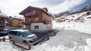 A multi-story building with balconies, a paved driveway, and a snowy mountain backdrop. - Chalet 'Malva' with Mountain View, Balcony and Wi-Fi (Livigno)