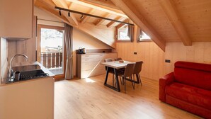 A wooden interior with a dining area, a red sofa, and a kitchen with a sink. - Chalet 'Malva' with Mountain View, Balcony and Wi-Fi (Livigno)