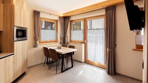Een moderne keuken met houten kastjes, een ingebouwde magnetron en een eethoek met een tafel en stoelen.