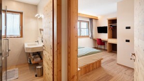 Een slaapkamer met een bed, bureau, televisie, douche en badkamer.