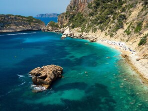 A coastal area with clear turquoise waters, rocky terrain, and a sandy beach with umbrellas. - Casa Guapa by Interhome (Jávea)