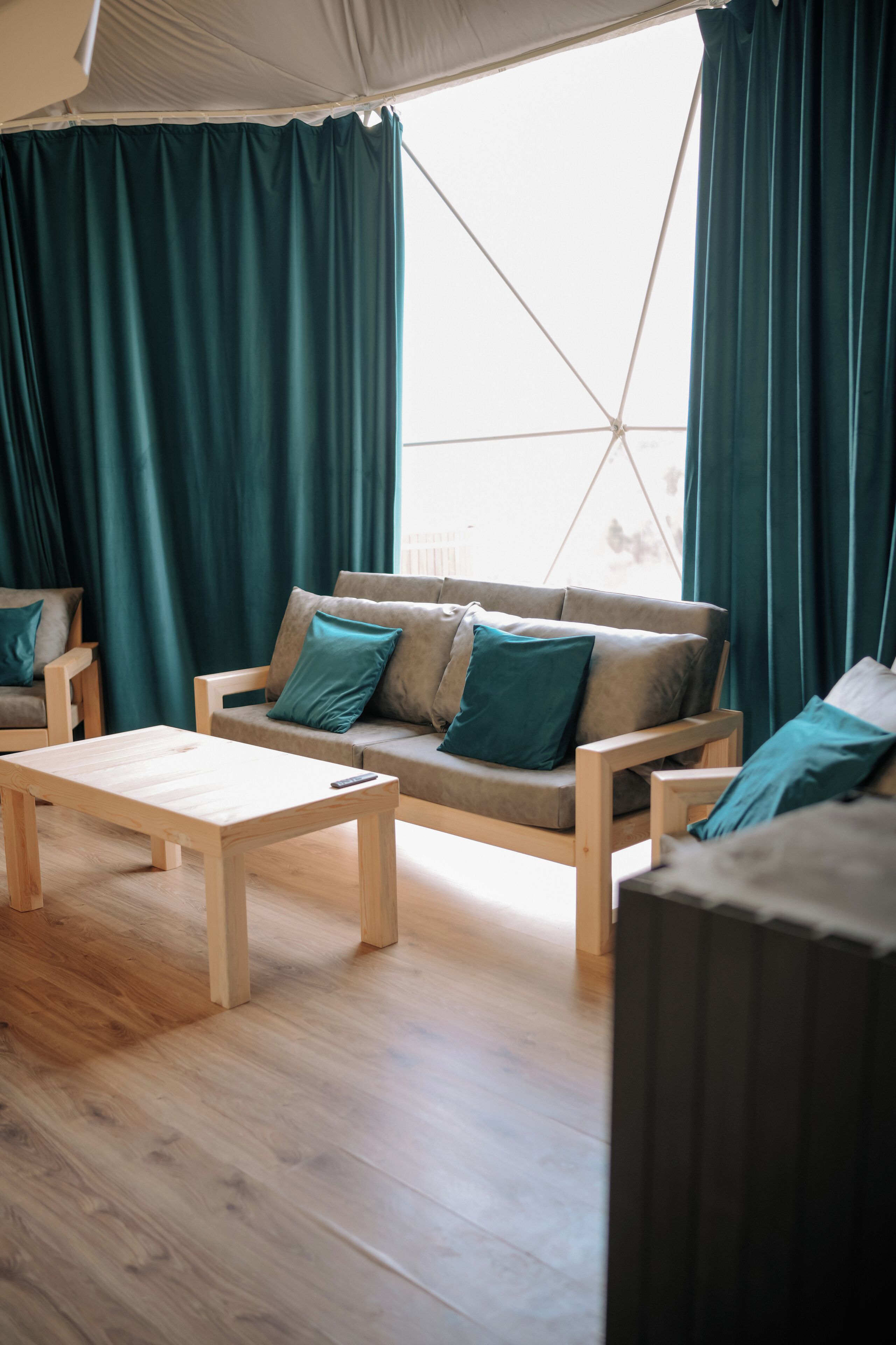 A room with a sofa, a wooden coffee table, and a large window with curtains.