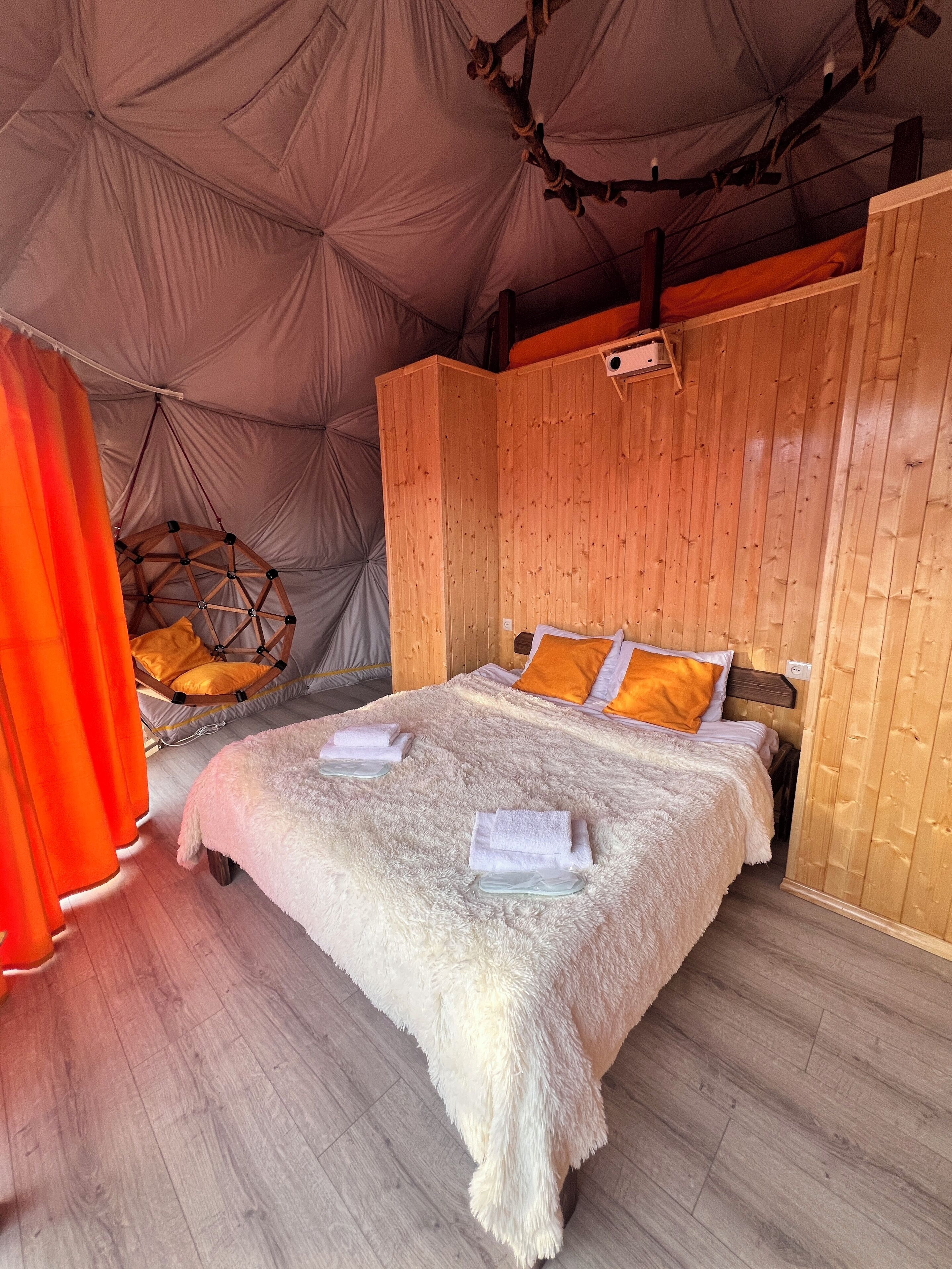 A cozy tented room with a wooden bed, a hanging chair, and a large window.