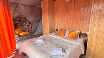 A cozy tented room with a wooden bed, a hanging chair, and a large window.
