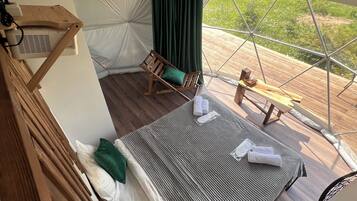 Alojamiento con tienda de campaña, una cama, una mecedora de madera y vistas al follaje exterior.