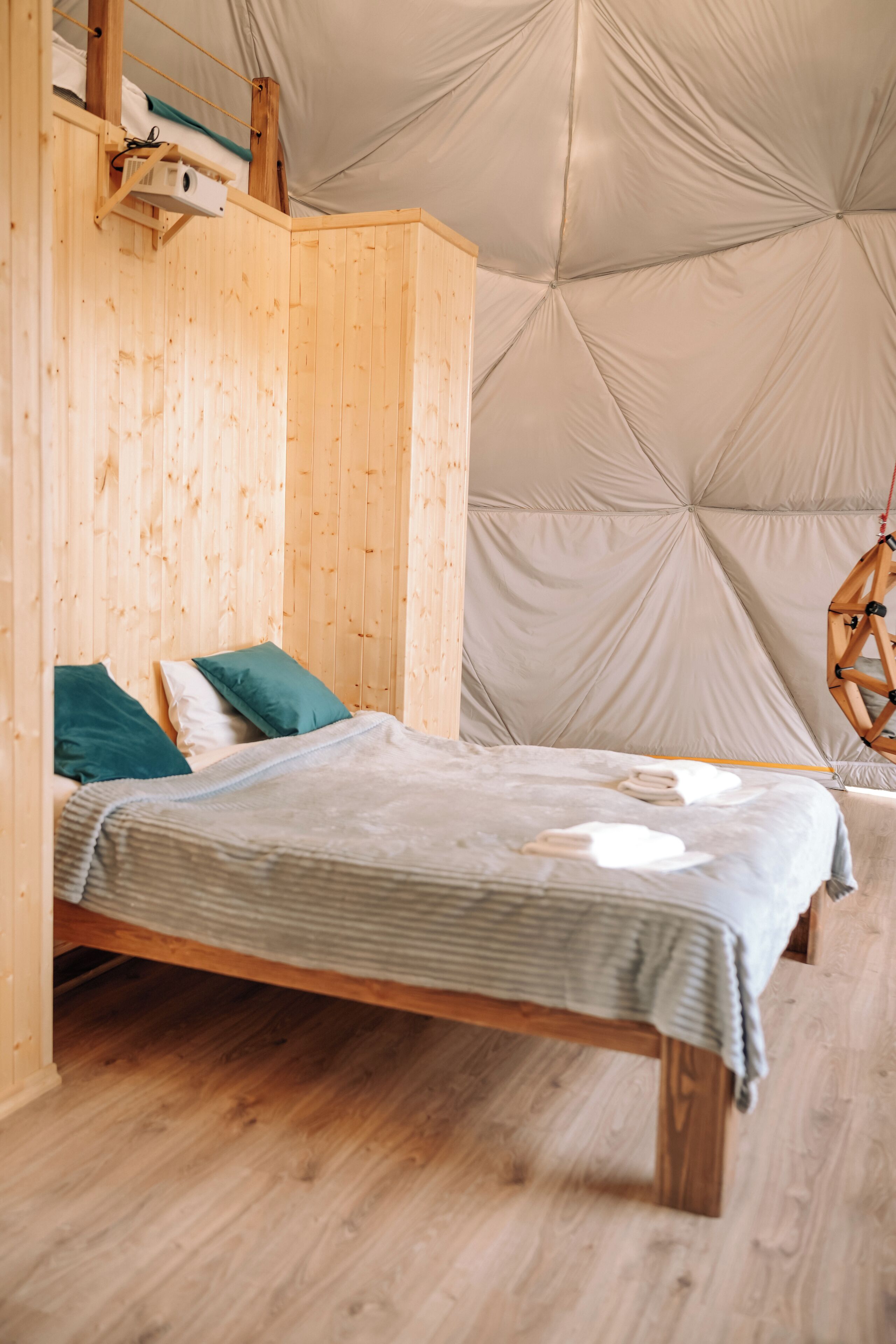 A wooden bunk bed with a striped blanket and pillows, a hanging chair, and a tent-like ceiling structure.