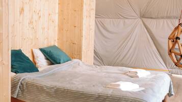 A wooden bunk bed with a striped blanket and pillows, a hanging chair, and a tent-like ceiling structure.