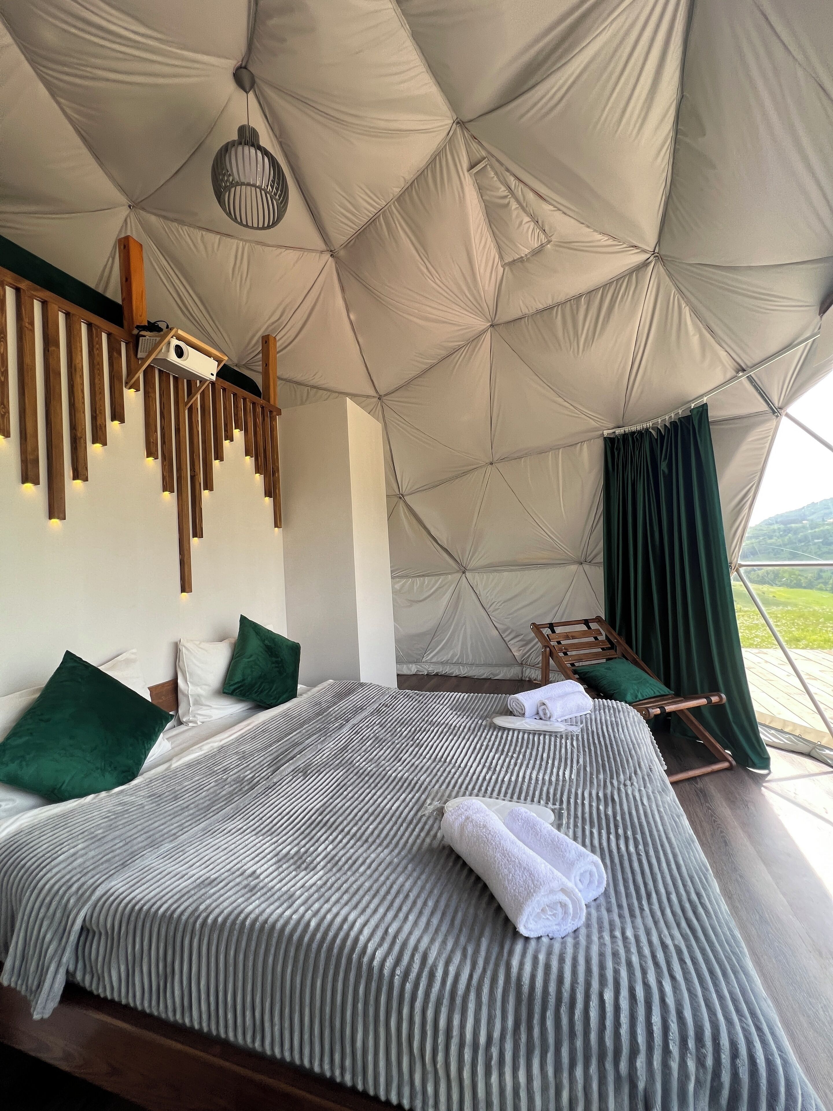 A tented room with a bed, pillows, a hanging light fixture, and a view of the outdoors.