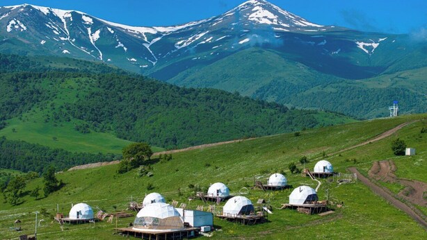 A landscape with several dome-shaped structures on a grassy hillside, with a mountain in the background. - GLAMPING PARK  (Shahumyan)