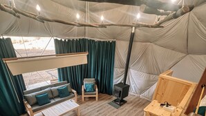 A tent interior with a sofa, a table, a sleeping area, and a wood stove. - GLAMPING PARK  (Shahumyan)