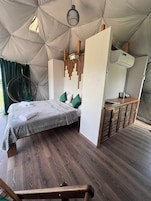 Una habitación tipo tienda de campaña con cama, sillón colgante y armarios de madera.
