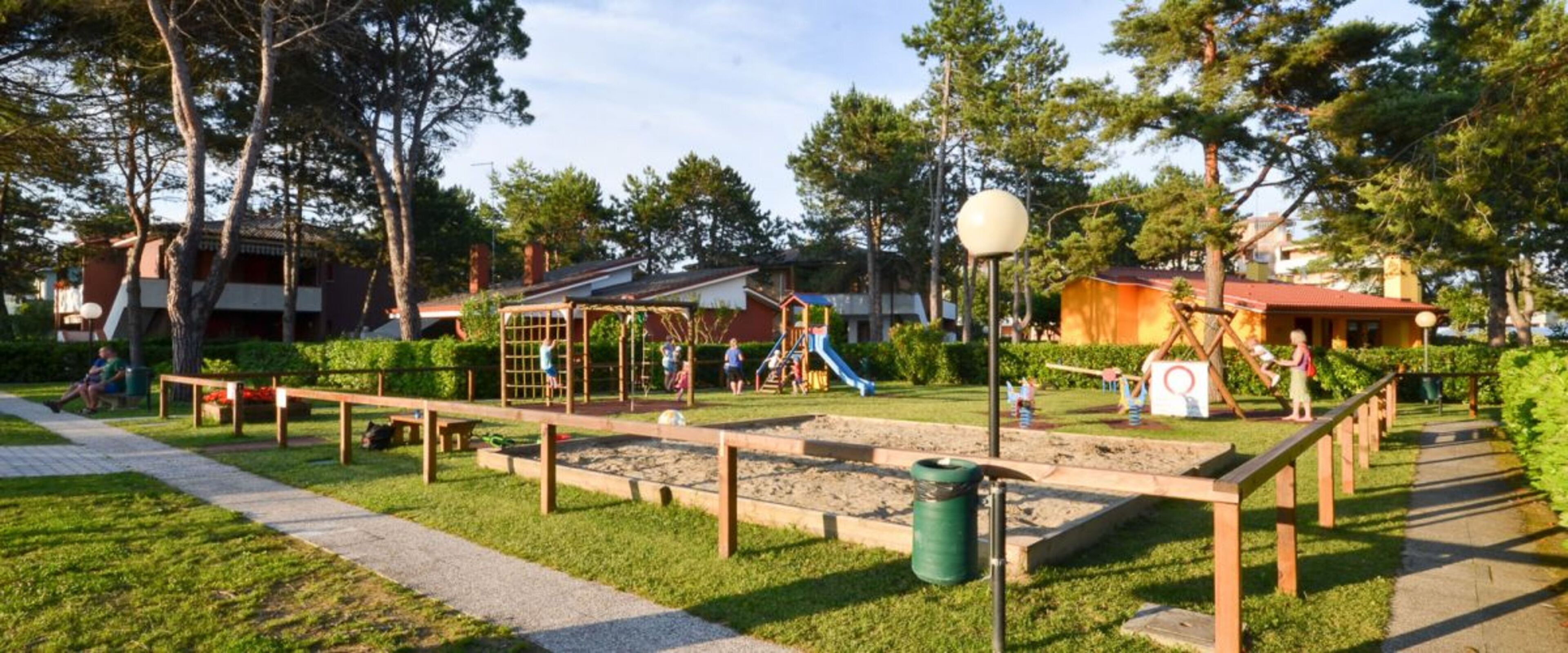A playground with various play structures, a walking path, and a green trash bin.