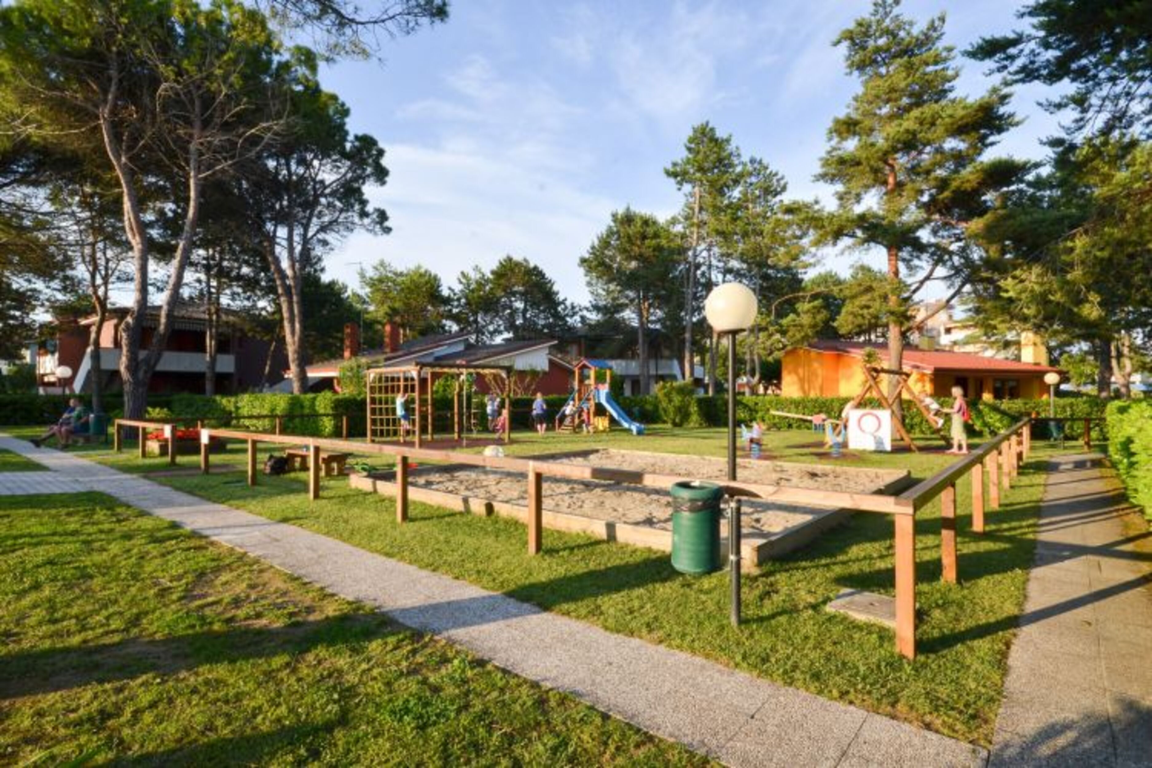 Un parque infantil con toboganes y estructuras para escalar, rodeado de árboles y un sendero.