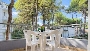 Ein Balkon mit weißen Plastikstühlen und einem Tisch, der auf einen Wohnbereich mit Bäumen und Gebäuden blickt.