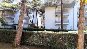 Ein Wohngebäude mit mehreren Balkonen, umgeben von Bäumen und einer gepflegten Hecke.
