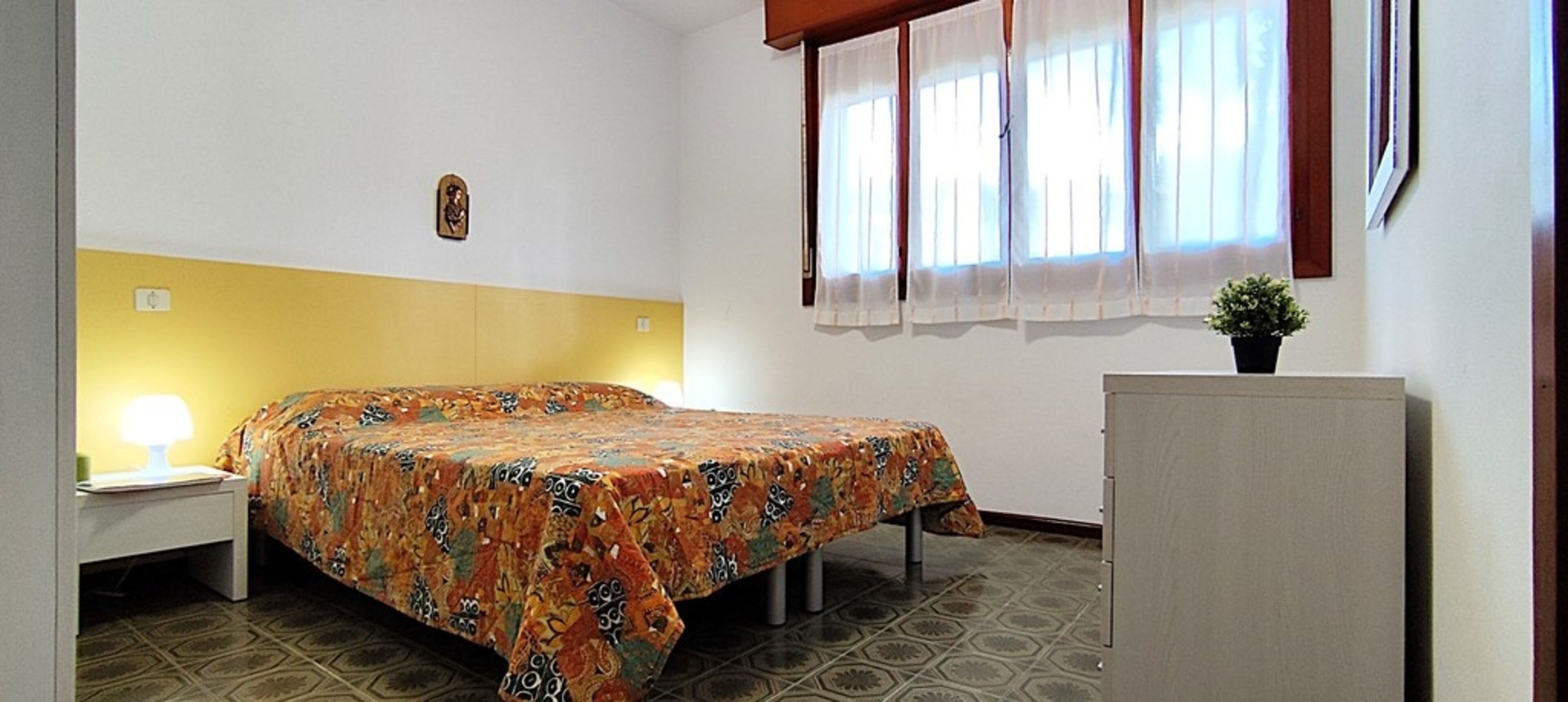 A room with a bed, a nightstand, a desk, a small cabinet, and a window with curtains.